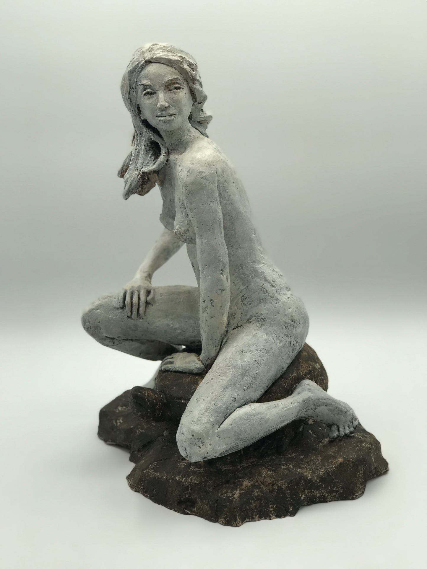 Side view of body and front view of face of a clay sculpture of a seated woman