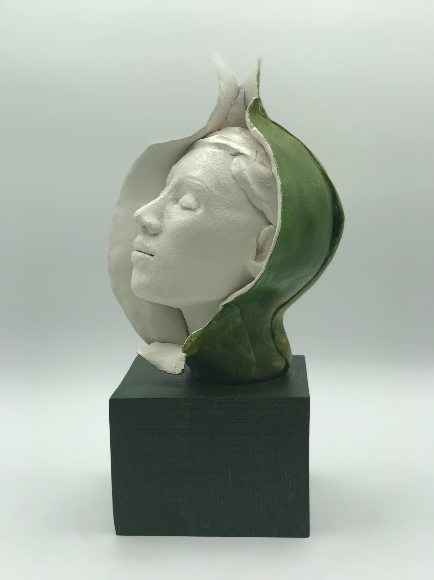 Clay sculpture of woman's head emerging from green bud. Eyes closed, peaceful expression.