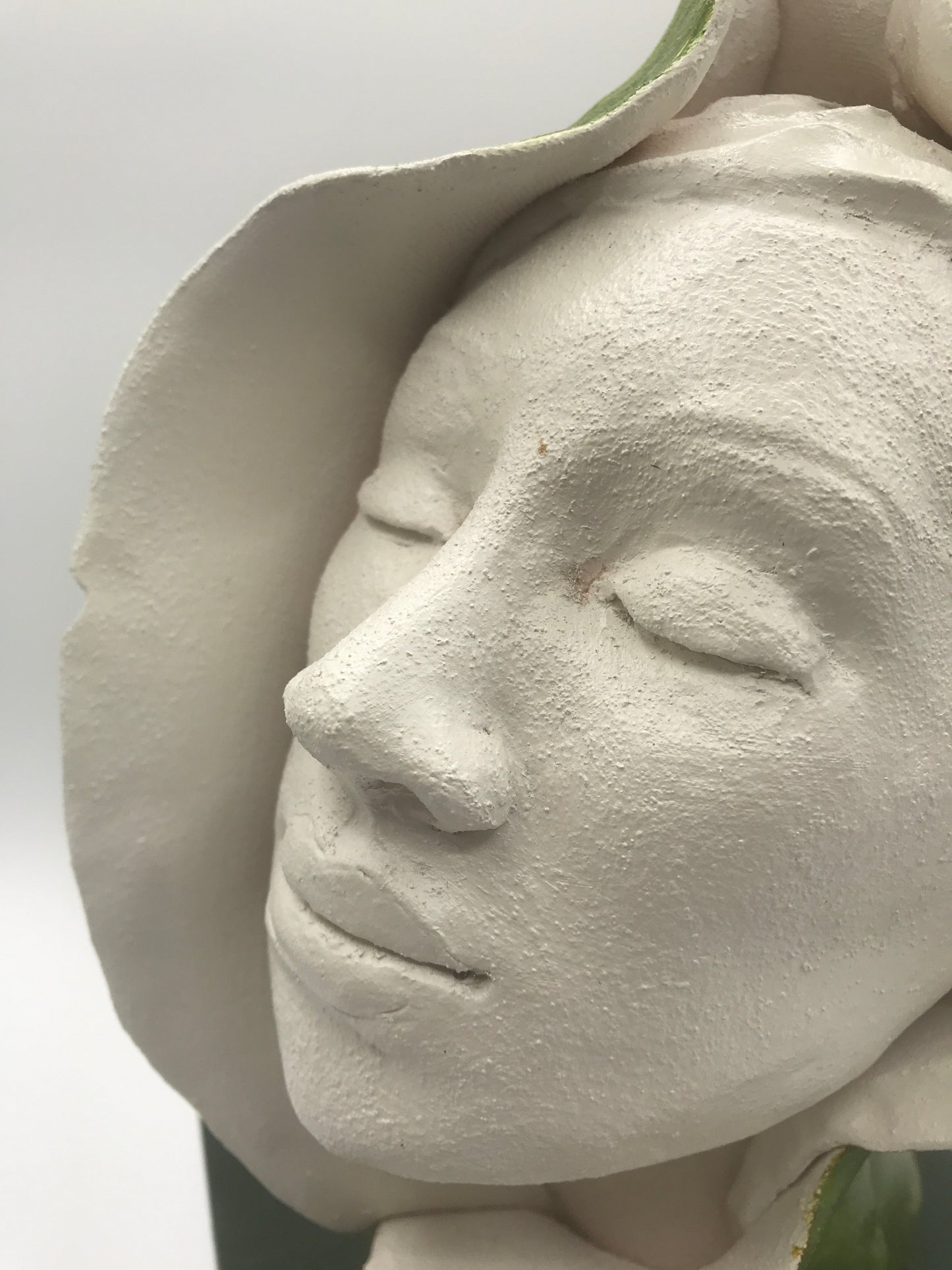 clay sculpture of woman's face emerging from a green bud. closeup shot showing grog - texture - in clay.